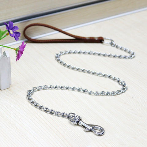 A metal traction chain for dogs with a PU handle, displayed on a wooden floor alongside a purple flower.